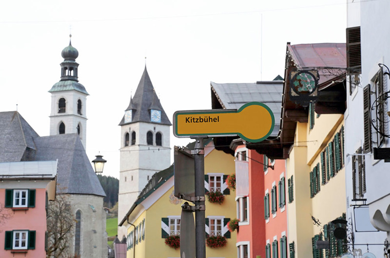 Kitzbühel på et skilt. Fargerike gamle hus og en kirke i bakgrunnen.