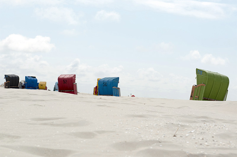 Sandstrand med fargerike, doble strandstoler med vegger og tak.