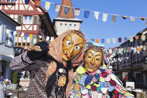 To maskekledde mennesker i en gate med bindingsverkshus: Karneval i Köln.